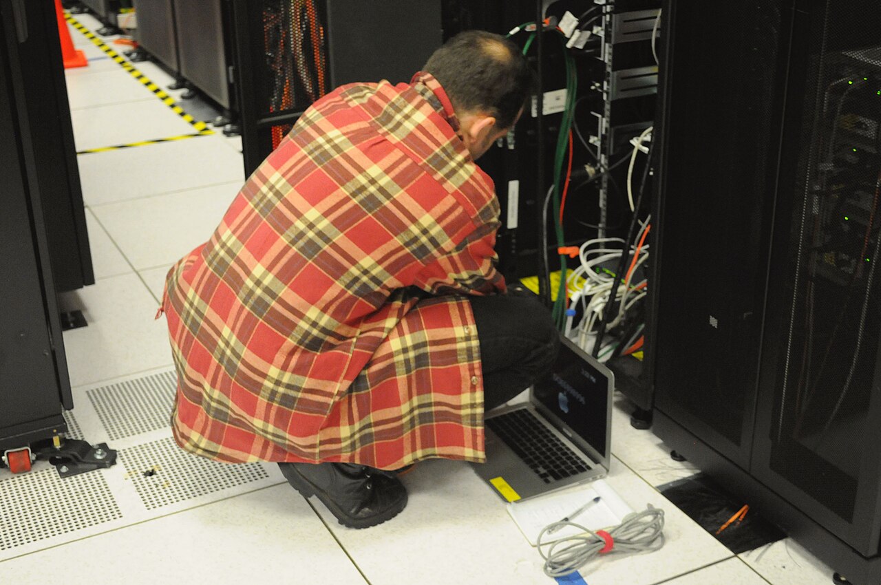 Technician working with a laptop in front of a server rack in a data center