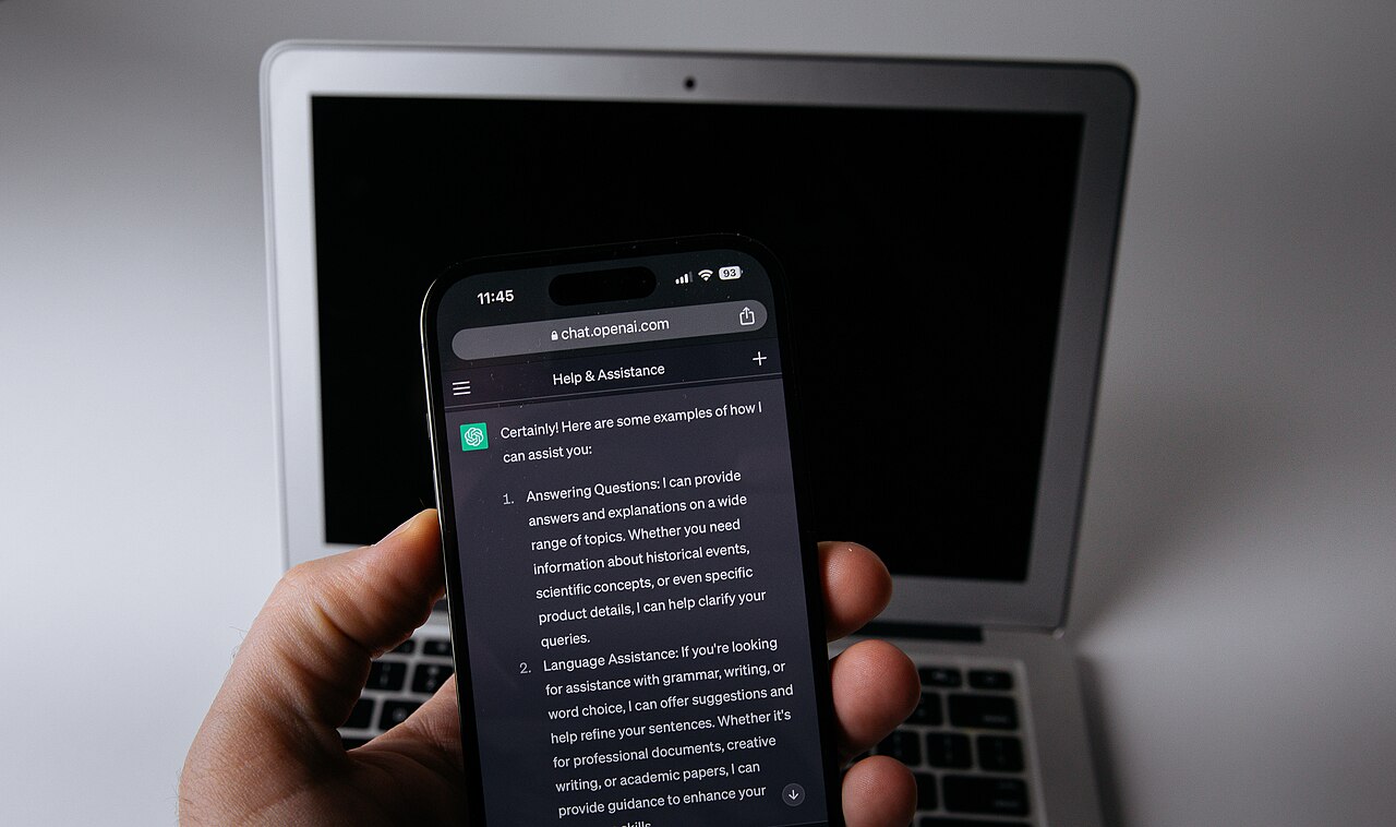 A mobile phone with the ChatGPT app open next to a laptop