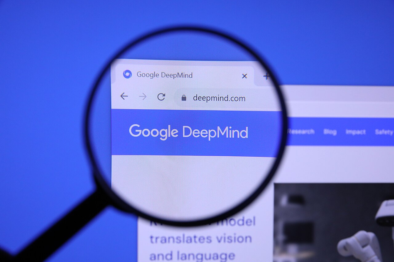 A magnifying glass held over a smartphone screen showing the Google DeepMind website homepage and logo