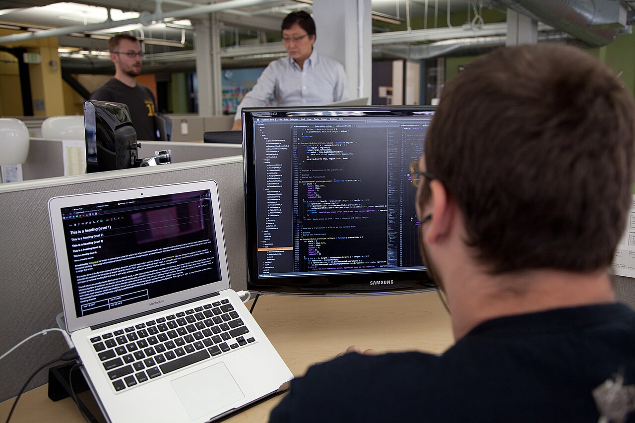 A developer coding at a computer, viewed from behind, in an office setting