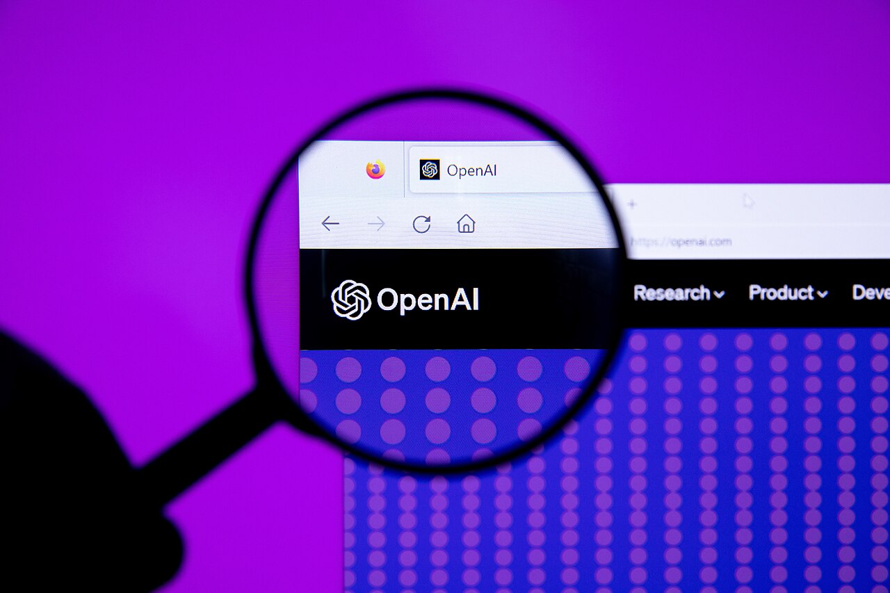 Das OpenAI-Logo auf einem Bildschirm, mit einer Lupe vergrößert