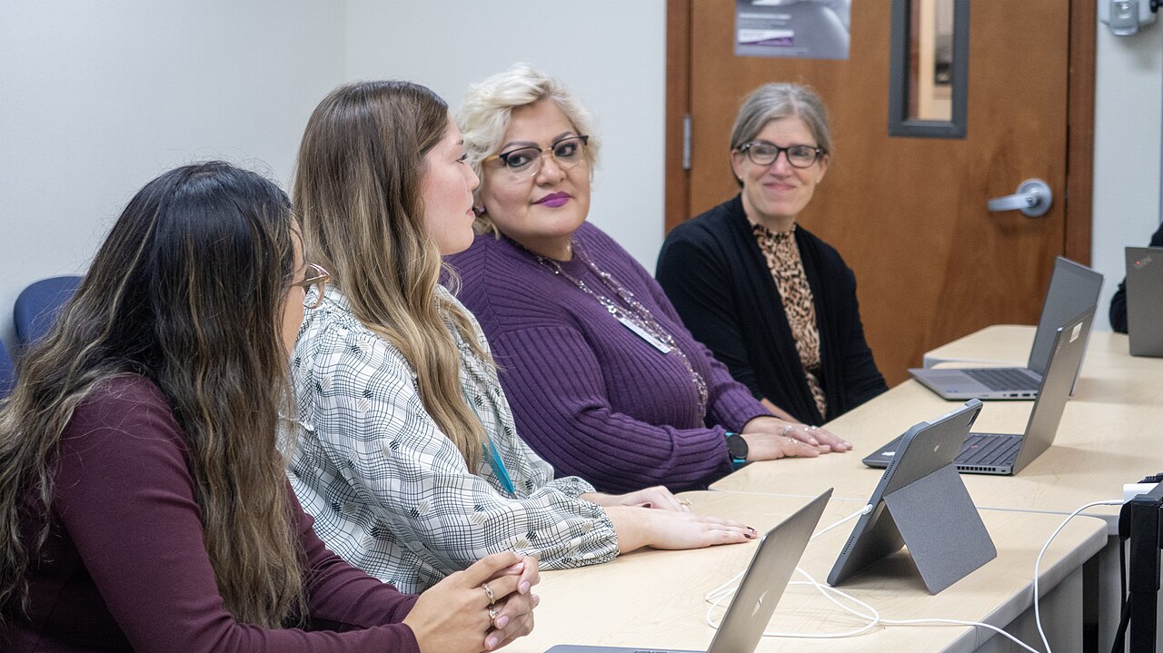 Four staff members sit around a meeting-room table with laptops and tablets.